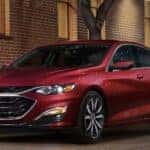 One of many popular used vehicles for sale near me, a red 2022 Chevy Malibu, is shown parked near a brick building.