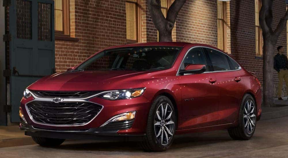 One of many popular used vehicles for sale near me, a red 2022 Chevy Malibu, is shown parked near a brick building.