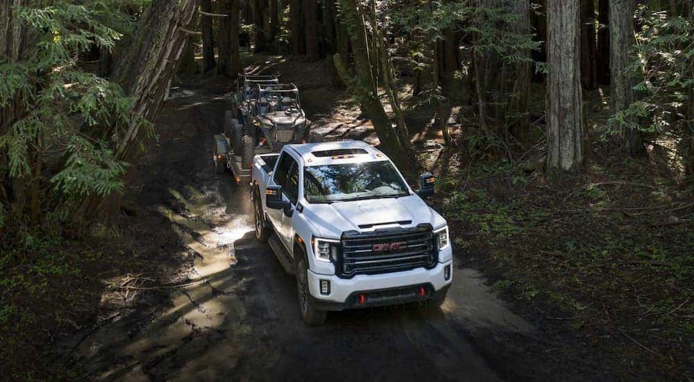Aerial view of a white 2021 GMC Sierra 2500HD towing ATVs through the woods.