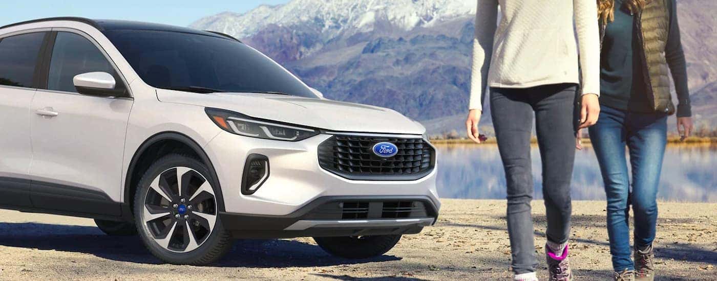 One of many popular used SUVs for sale, a white 2023 Ford Escape Platinum, is shown parked near two people walking.