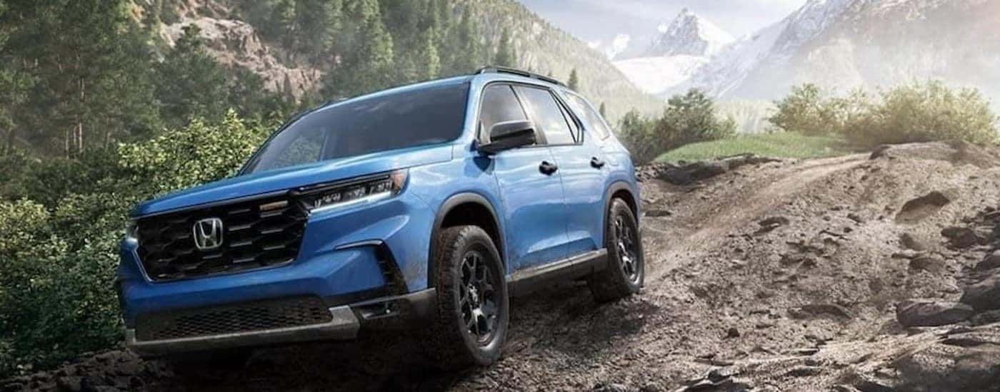 A blue 2023 Honda Pilot TrailSport is shown driving off-road.