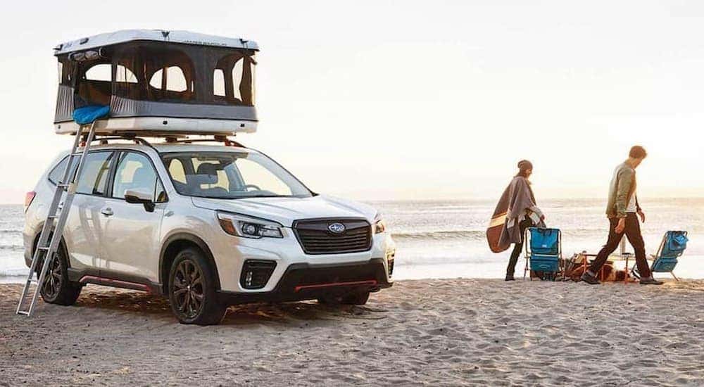 A white 2021 Subaru Forester parked on the beach with a pop-up tent on the roof.