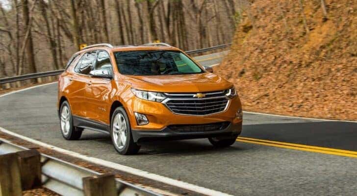An orange 2019 Chevy Equinox is shown driving to view used cars for sale near Chapel Hill.
