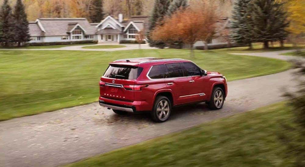 A red 2023 Toyota Sequoia is shown driving near a house.