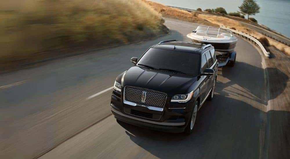 A black 2022 Lincoln Navigator is towing a boat past a lake.