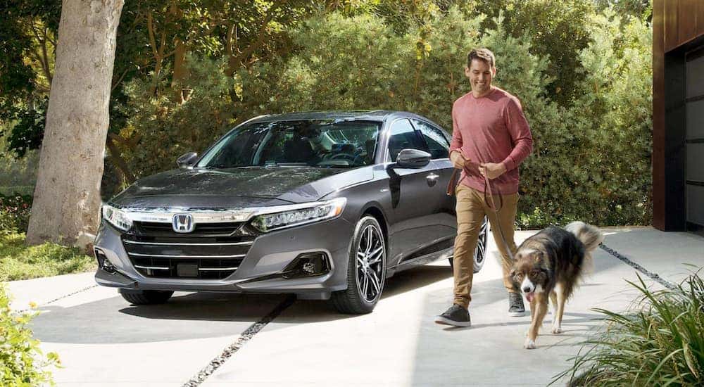 A man walking his dog past a silver 2021 Honda Accord Hybrid Touring parked in the driveway.