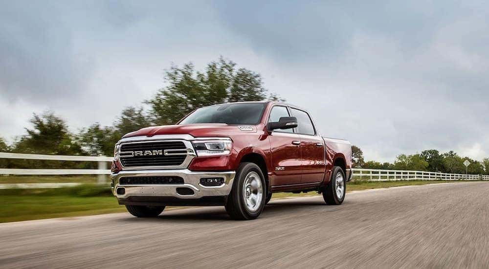 A red 2020 Ram 1500 is shown driving near a fence after viewing used cars for sale near Raleigh.