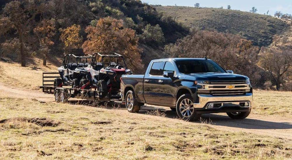 A black 2020 Chevy Silverado 1500 towing a trailer with ATVs through a field.