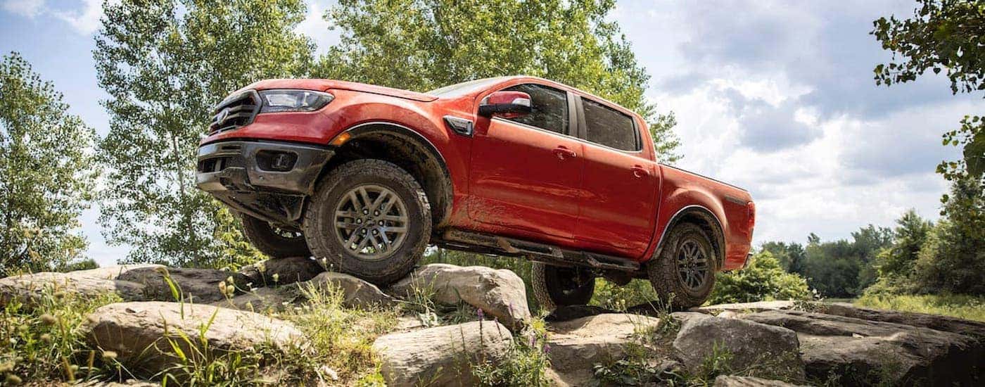 Side angle view of an orange 2021 Ford Ranger Tremor Lariat parked off-road on boulders.