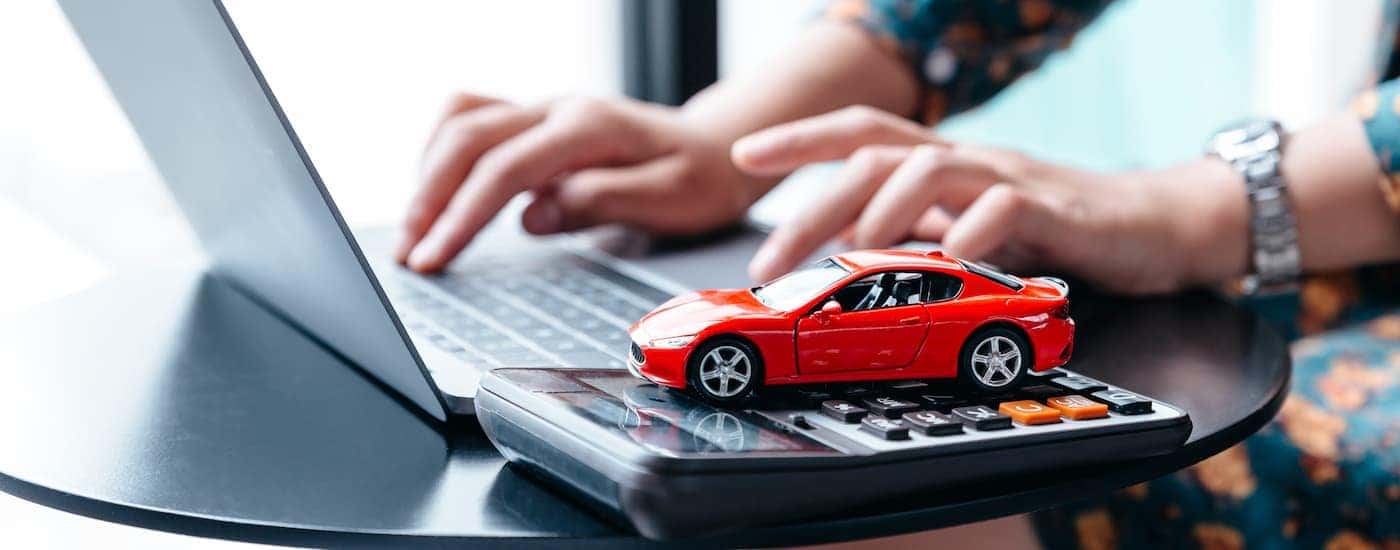 A person is using a laptop with a red toy car on a calculator.