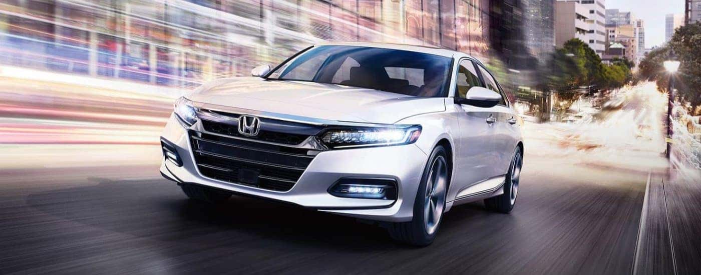 A white 2020 Honda Accord Touring driving down a road from a used car dealership near Chapel Hill.