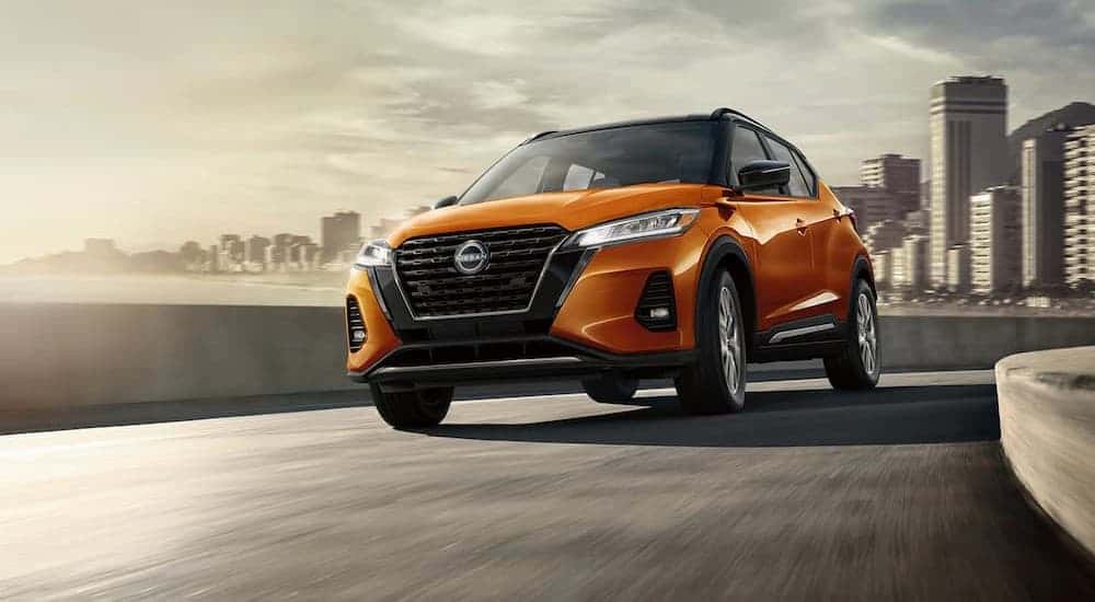 An orange 2024 Nissan Kicks driving near a city.