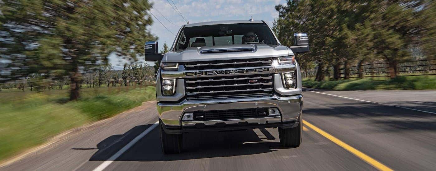 A silver 2020 Chevy Silverado 2500 HD Z71 is shown driving on a tree lined road.