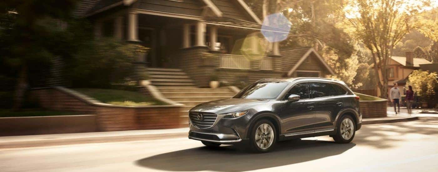 A grey 2019 Mazda CX-9 driving on a sunny suburban street