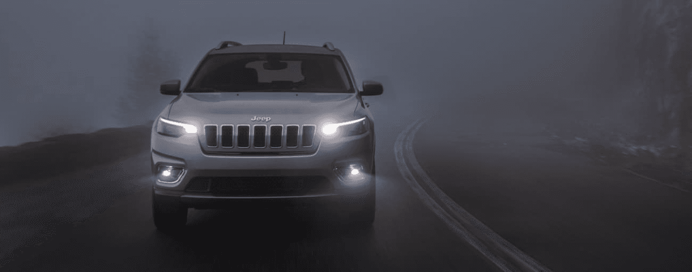 A grey 2020 Jeep Cherokee is shown driving through fog after searching for used vehicles for sale