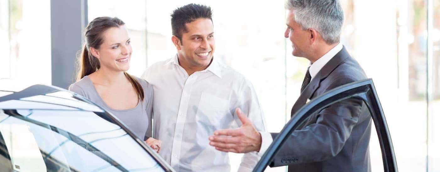 A salesperson helps two customers who came in to sell their car