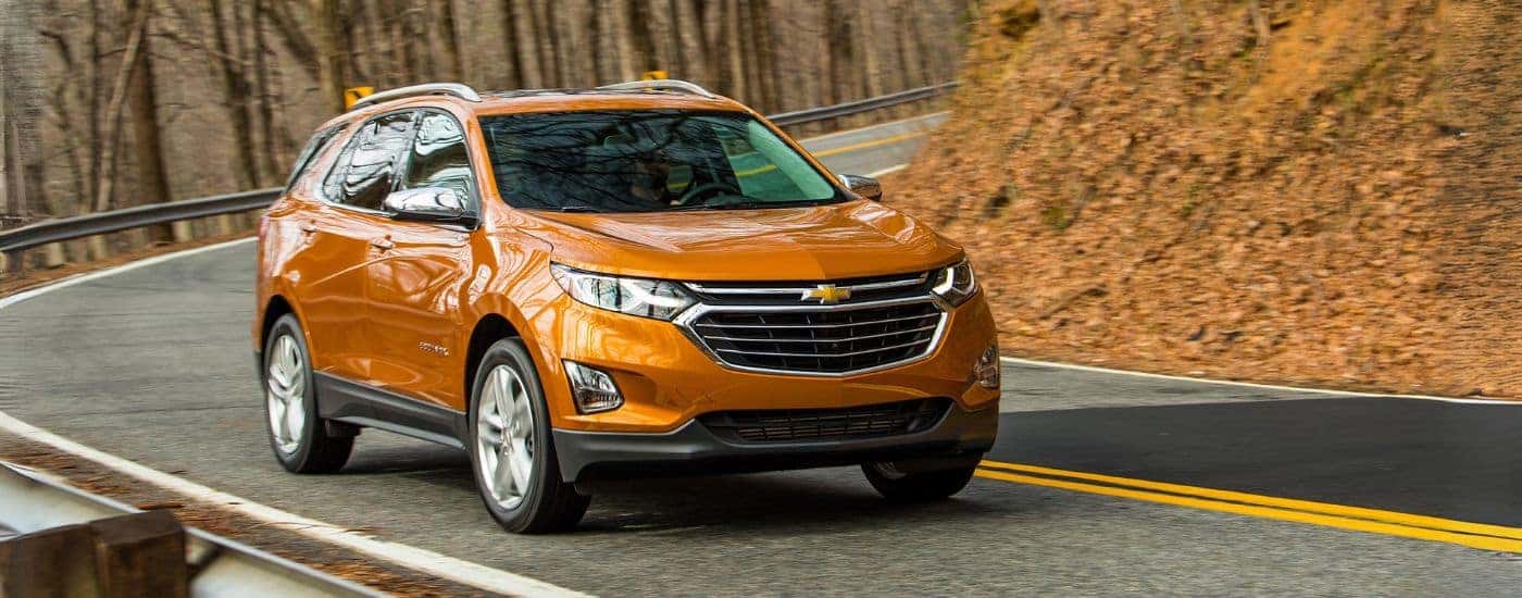 An orange 2019 Chevy Equinox is shown driving to view used cars for sale near Chapel Hill.
