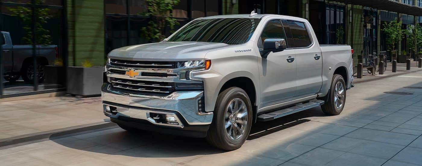 A silver 2019 Chevy Silverado 1500 is shown driving on a city street after looking at used cars near Raleigh, NC.