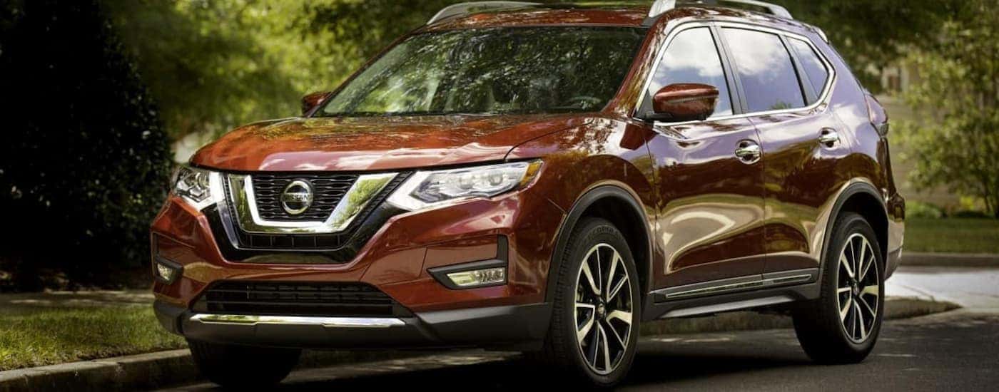 A popular used SUV for sale in Durham, NC, a dark red 2019 Nissan Rogue, is parked in front of a house.