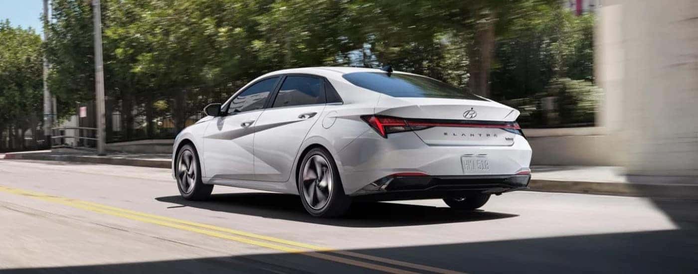 A white 2021 Hyundai Elantra Hybrid is shown parked near a used car dealership.