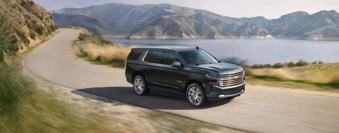 A grey 2022 Chevy Tahoe driving on a winding road near a lake.