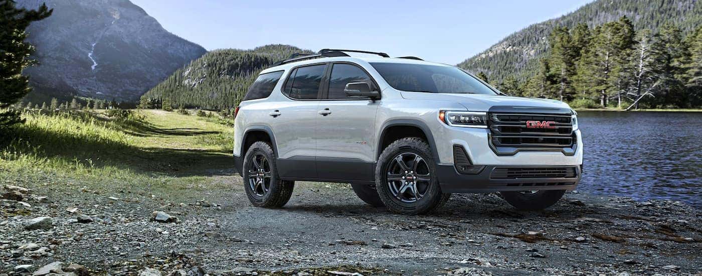 A white 2023 GMC Acadia AT4 is shown parked near a lake.
