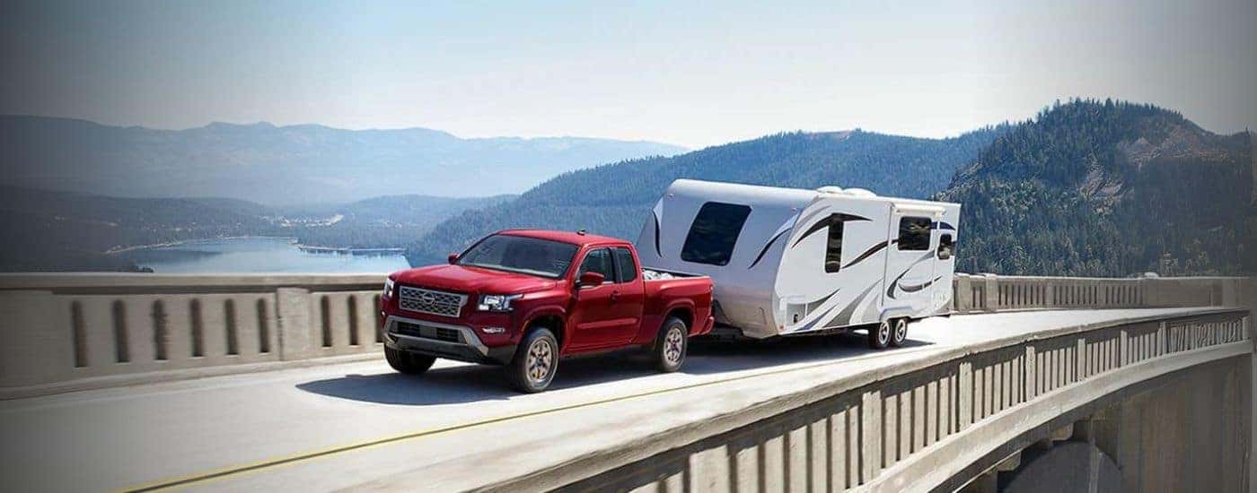 A red 2024 Nissan Frontier is shown towing a trailer on a bridge.