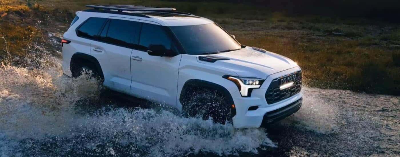 A white 2023 Toyota Sequoia is shown driving off-road after viewing used cars for sale near Mebane.
