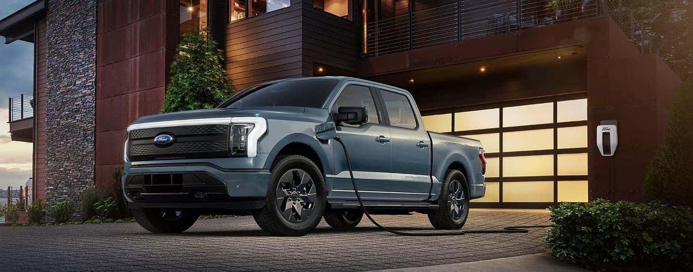 A blue 2023 Ford F-150 Lightning plugged into a home charger.