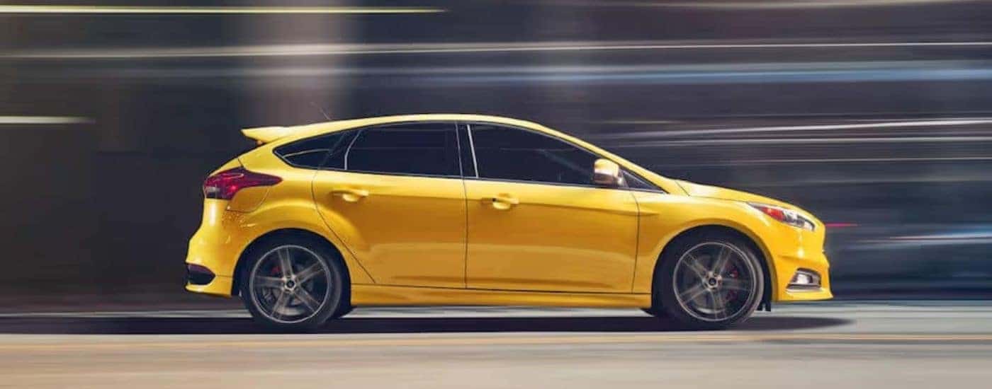 A yellow 2018 Ford Focus ST is shown from the side driving down a city street.