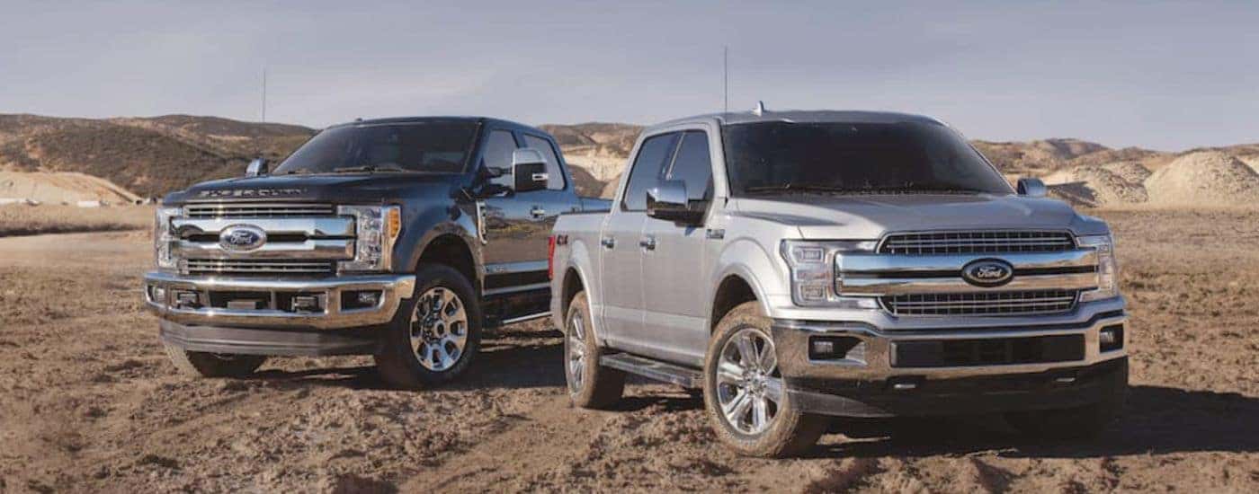 A black 2019 Ford F-250 Super Duty and a silver F-150 are parked in a dirt field.