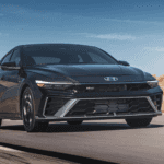 A black 2025 Hyundai Elantra N driving on a desert highway under a blue sky.