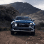 A blue 2025 Hyundai Tucson driving on a dirt road with mountains behind.