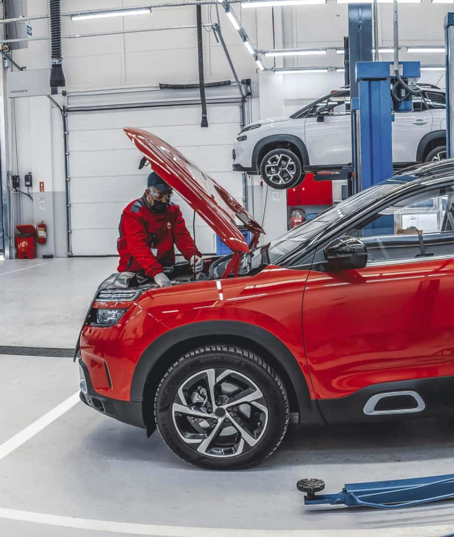 Auto mechanic performing engine diagnostic on Red Hyundai SUV in repair shop