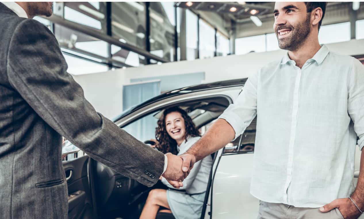 A salesperson shakes hands with a customer as they get into a new car.
