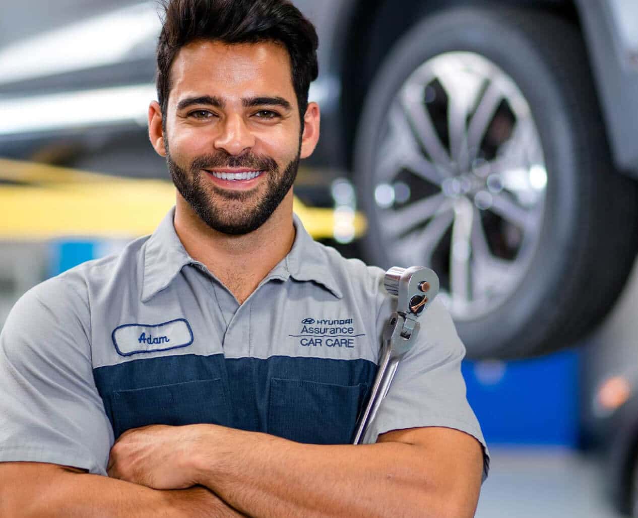 A Hyundai Certified Technician holding a wrench crosses his arms and smiles.