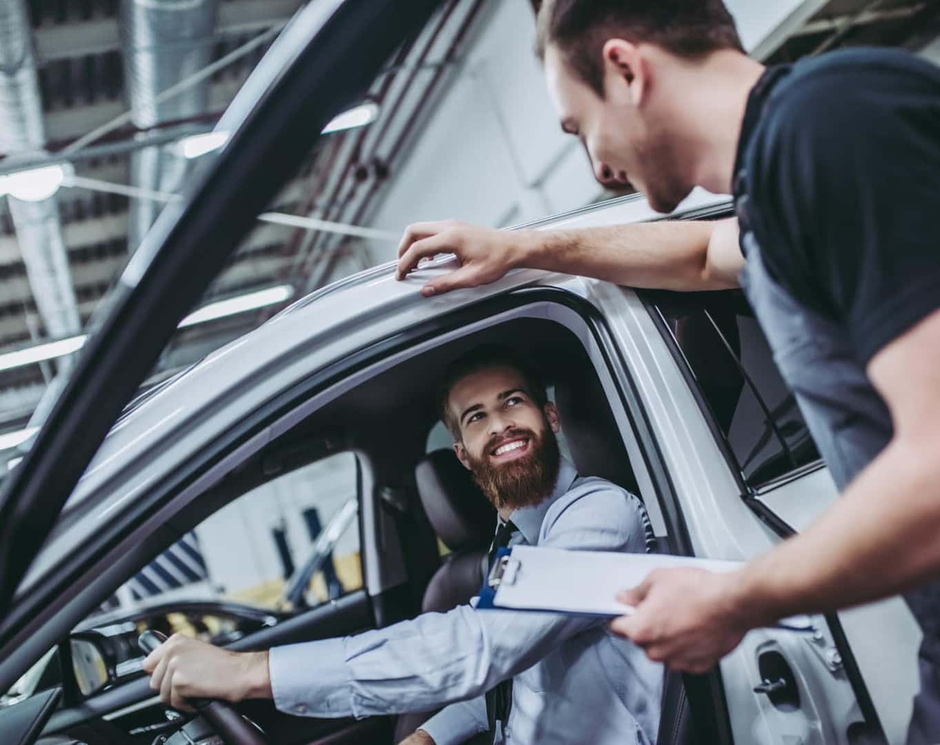 Customer speaking with a dealership representative while seated in a vehicle inside a service center.
