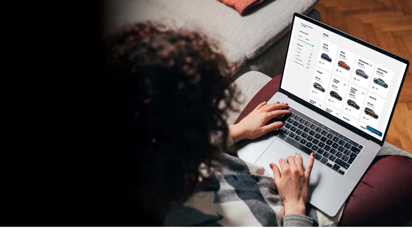 Over-the-shoulder view of a person using a laptop to browse the Hyundai SUV lineup on an online vehicle configurator webpage.