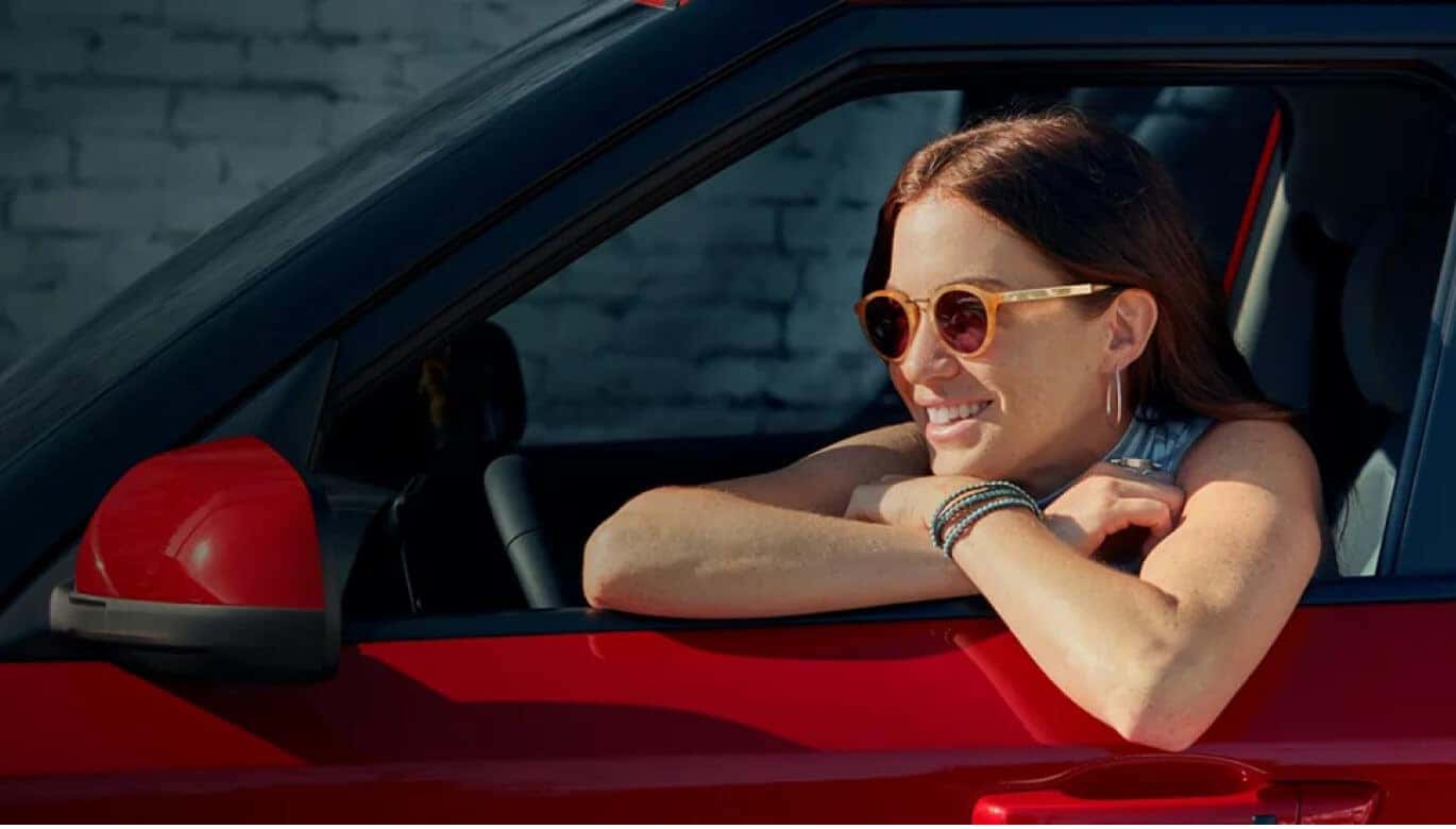 Close-up side profile view of a Hyundai Kona SEL in Ultimate Red showing a smiling woman wearing sunglasses.
