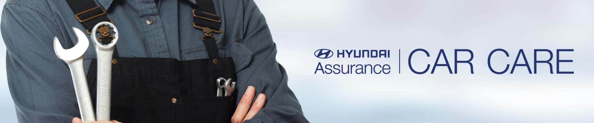Mechanic with arms crossed holding wrenches, featuring the Hyundai Assurance Car Care logo.