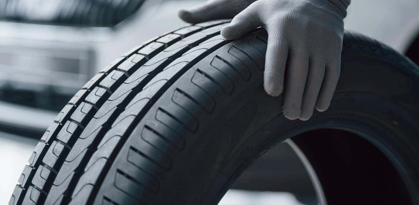 Close-up view of a technician in grey gloves inspecting a black car tire in a service bay.