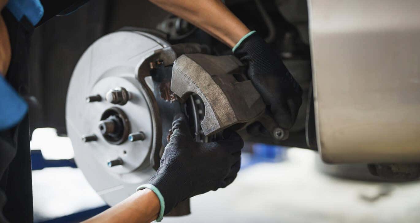 Close-up view of a mechanic installing a brake caliper on a rotor in a service shop.
