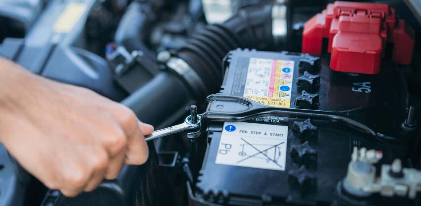 Close-up view of a hand tightening a bolt on a car battery in a car engine.