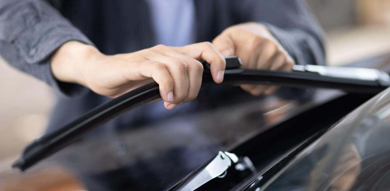 Close-up view of hands installing a new windshield wiper blade on a car windshield.