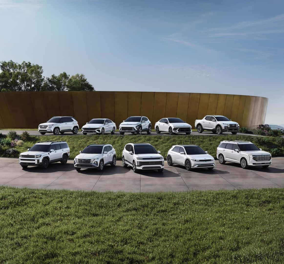 Wide view of the full 2026 Hyundai lineup all in white parked side-by-side in a modern grass-lined parking lot.