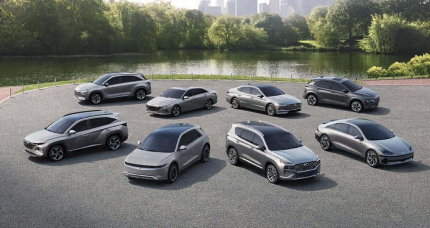 Wide view of the full 2023 Hyundai lineup in black, silver and dark gray parked in an urban park near a pond.
