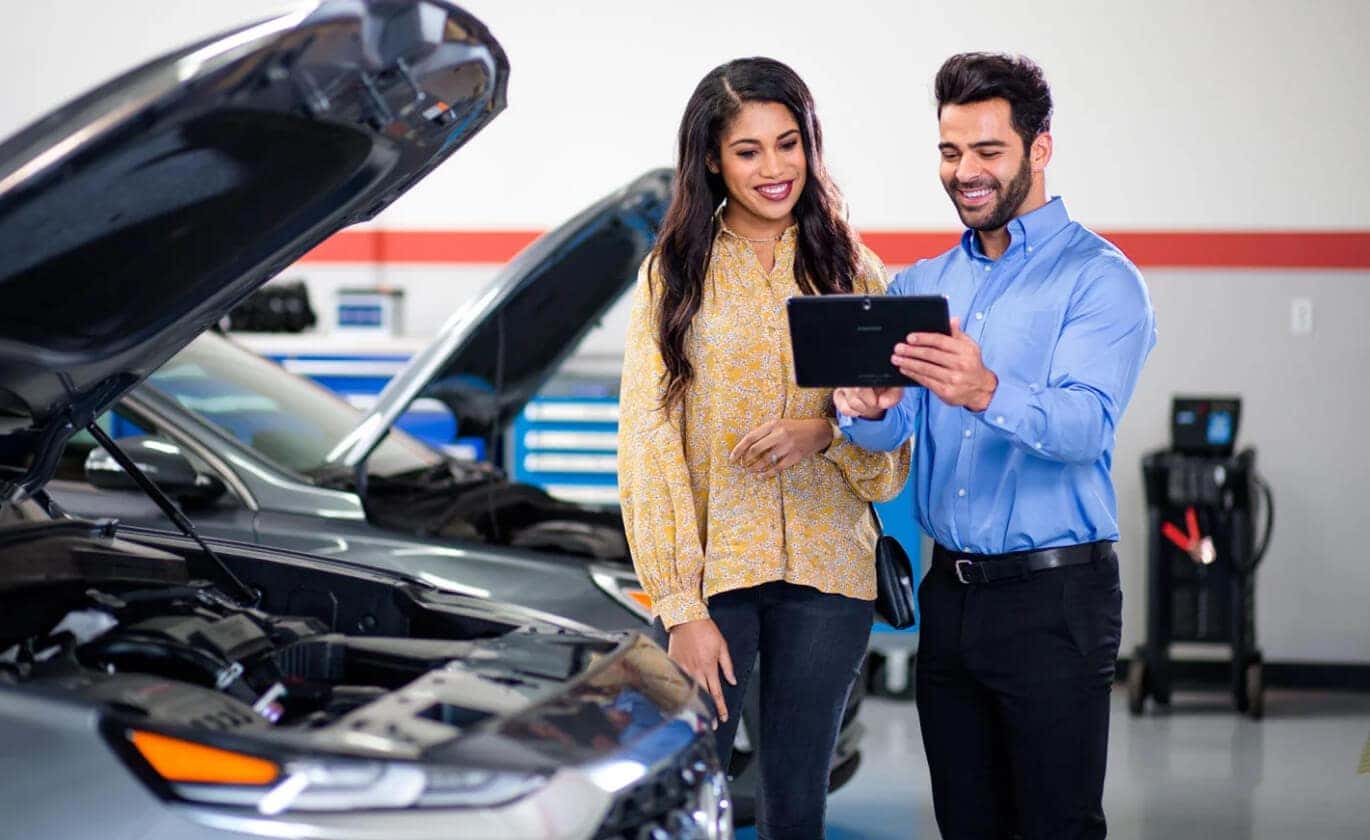A Hyundai Service specialist holds up a tablet while assisting a smiling customer. 