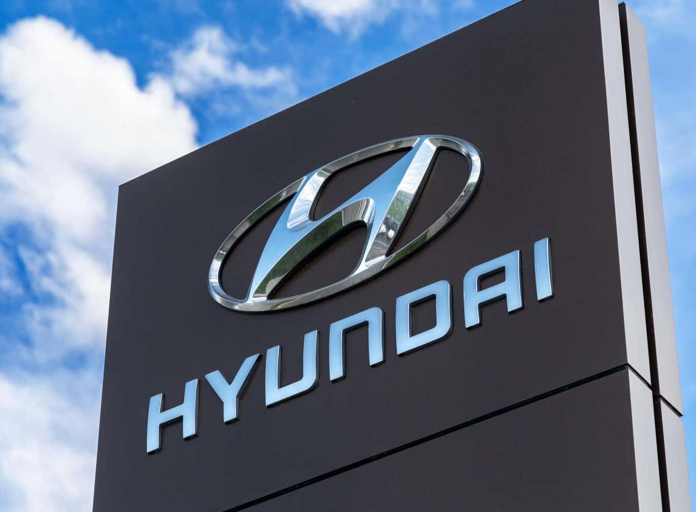 Low angle perspective view of a Hyundai dealership sign against a cloudy blue sky background on a sunny day.