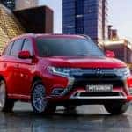 A red 2020 Mitsubishi Outlander PHEV is parked in front of city buildings.
