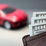 A closeup of a wallet with hundred dollar bills is in front of a red car found at Used Car Dealership Near Me.